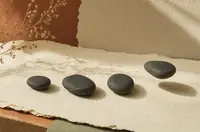 Four dark smooth stones in a row on handmade cream paper